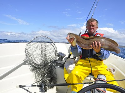 Fisherman with ling fish on motorboat.