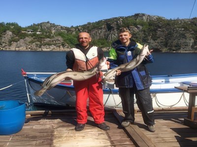 Two guests holding ling fish on dockside.